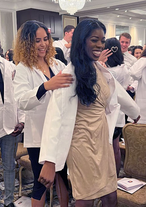 Medical students help each other don their white coats at the white coat ceremony