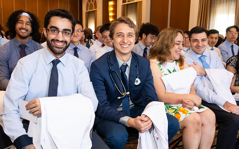 Four DO students smile with their white coats during the ceremony