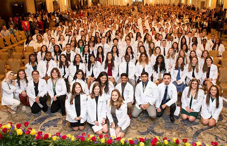 Large group photo of the PCOM DO Class of 2027 smiling in the ballroom during the white coat ceremony
