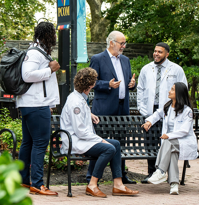 PCOM President Dr. Jay Feldstein talking with osteopathic medical students in a college courtyard