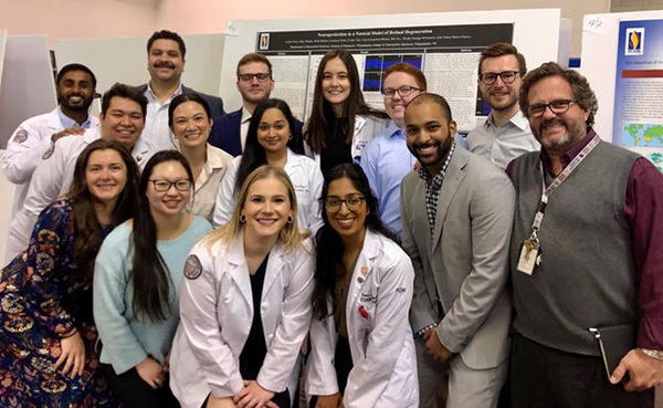 Dr. Bravo Nuevo smiles with a group of PCOM research students as they present their research posters