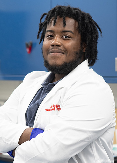 Cabrini student Steven Morency smiles in a lab coat in a PCOM research lab