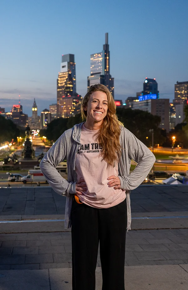 PCOM psychology student Benni Litman (MS '27) smiling while posing on top of the Philadelphia Art Museum steps with the city skyline in the background at dusk