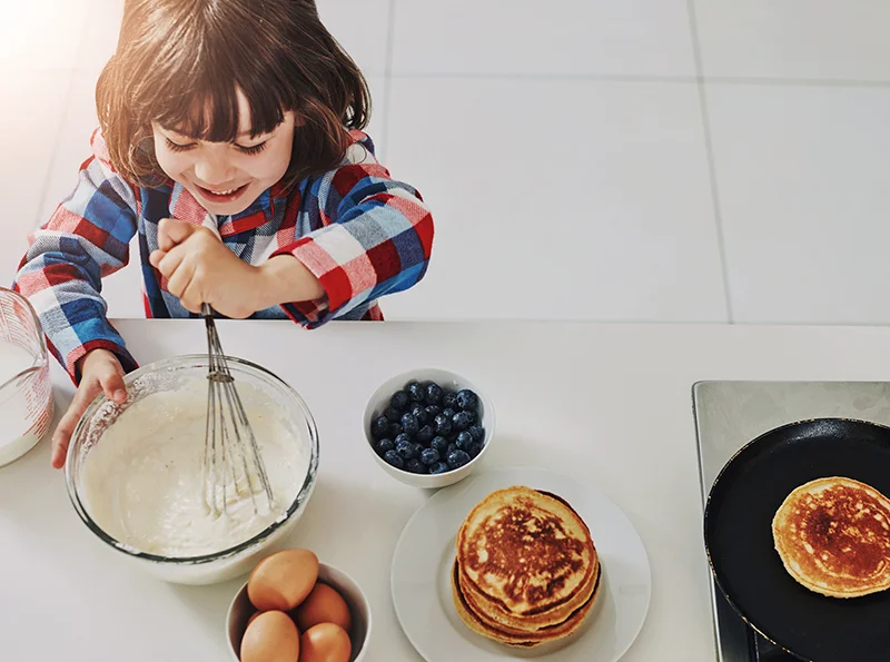 A young child smiling as they whisk batter on a kitchen countertop while making pancakes
