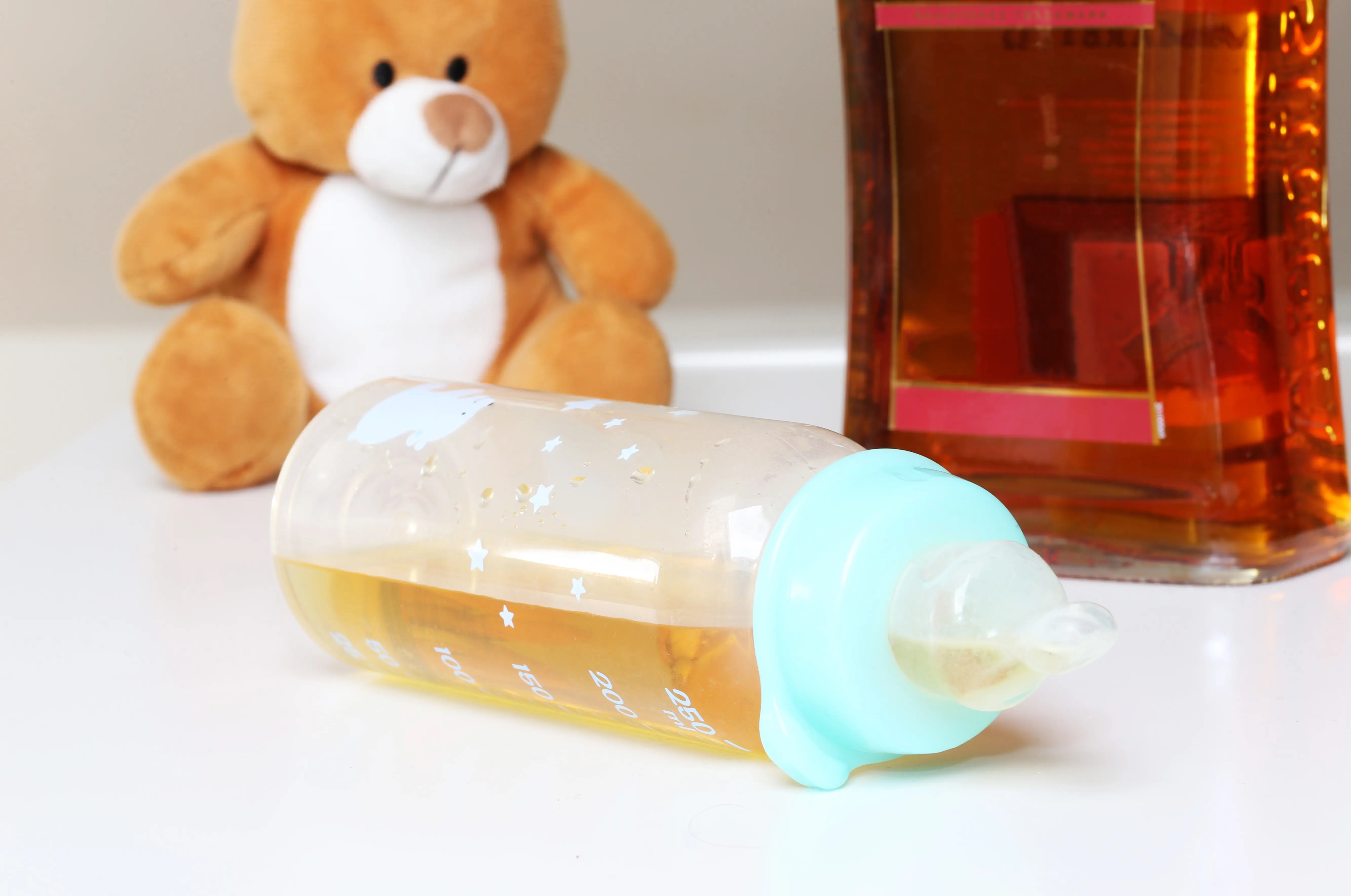 A baby bottle is shown with a teddy bear and bottle of liquor.