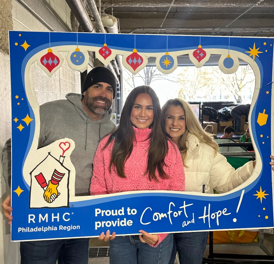 PCOM DO student Ellie Koerner smiles with her mom and dad in a garage during a toy drive collection