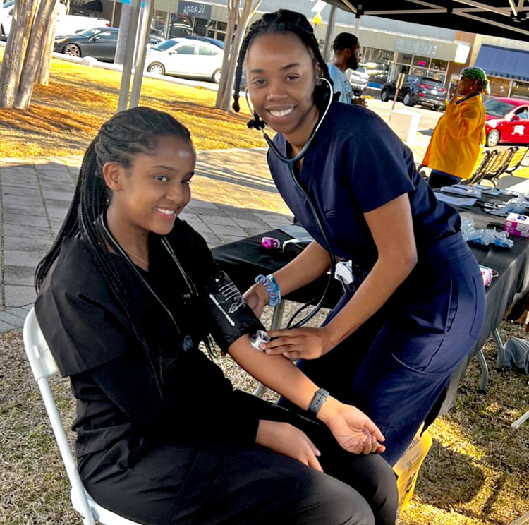 Female med student smiles and takes takes blood pressure of a Moultrie citizen under a canopy