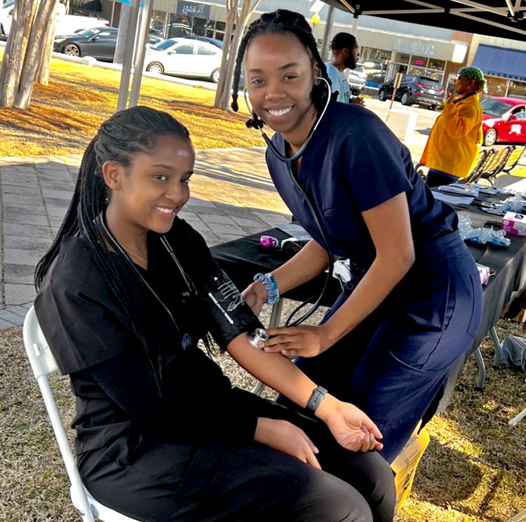 Female med student smiles and takes blood pressure of a Moultrie citizen under a canopy