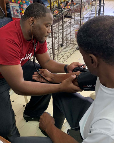 PCOM medical student records blood pressure of local community member at barbershop