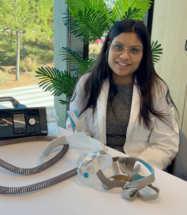 PCOM South Georgia medical student Neeti Shirke smiles in front of a PAP device in an office