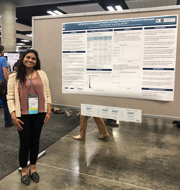 DO student Neeti Shirke stands and smiles in front of her research poster display on PAP devices and sleep apnea treatment