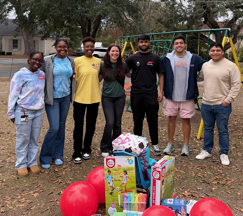 PCOM South Georgia medical students smile in a park during a charity drive event with their toy donations in the foreground