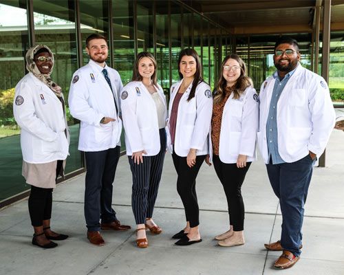 PCOM medical student in white coats standing in front of glass building