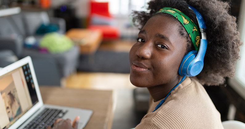 High school student wears headphones and uses a laptop for online learning in her home