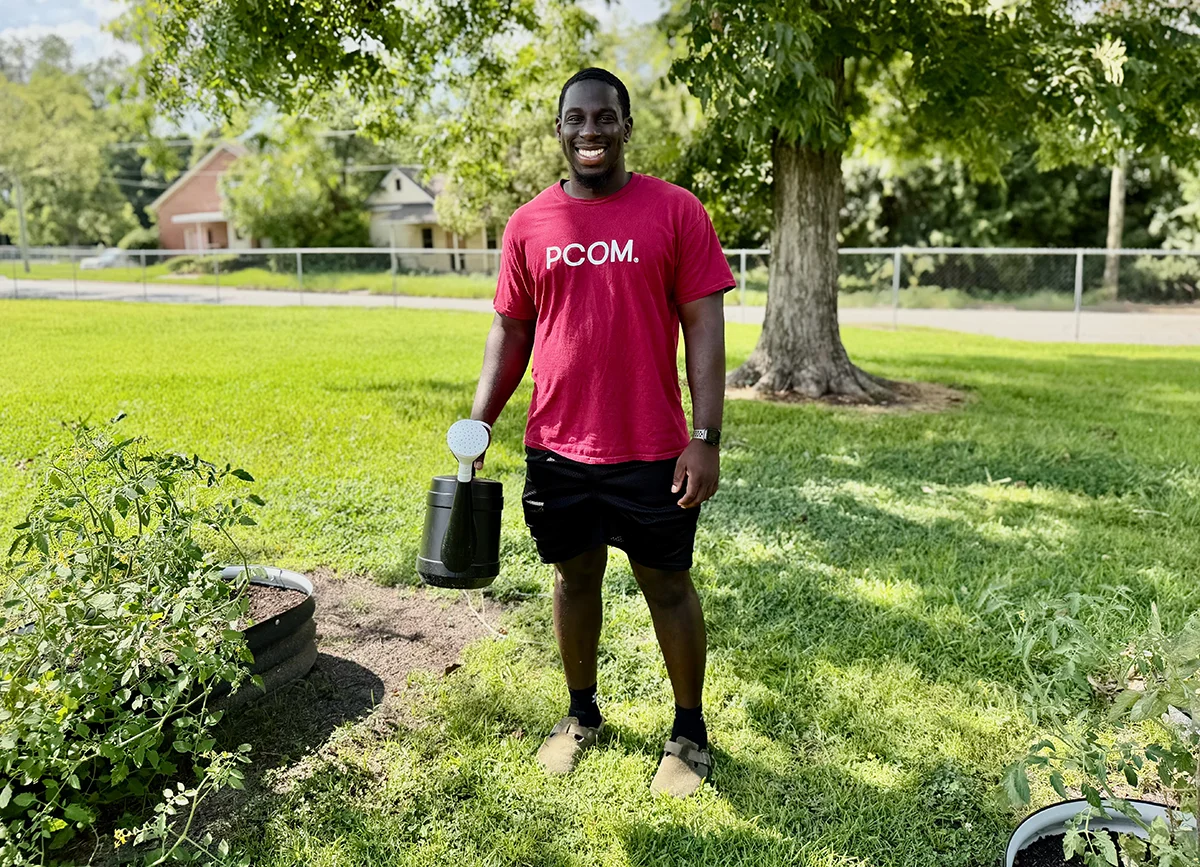 Medical student, Barry Francis, holds a watering can while standing next to a raised garden bed