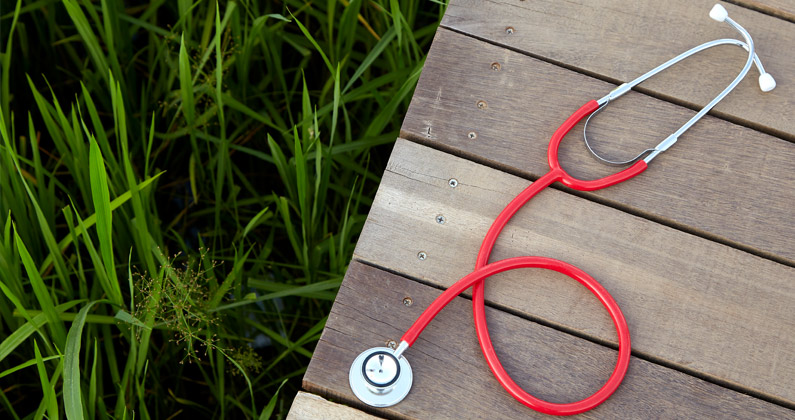 A stethoscope sits on a wood plank walkway on top of a green grass field.