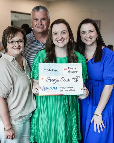 DO student surrounded by family holds up Match Day sign