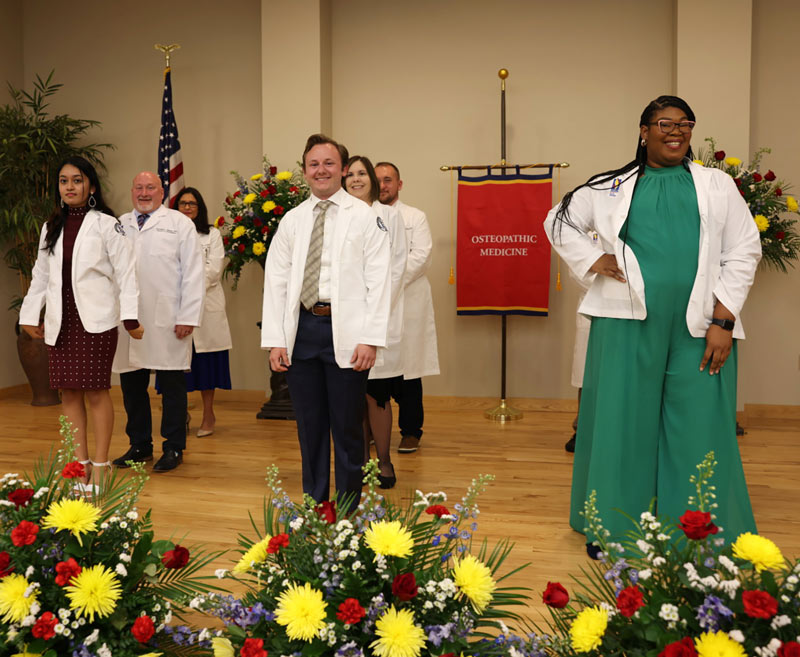 A group of students take a moment to pose for the camera immediately after receiving their coats from faculty members during PCOM South Georgia’s white coat ceremony