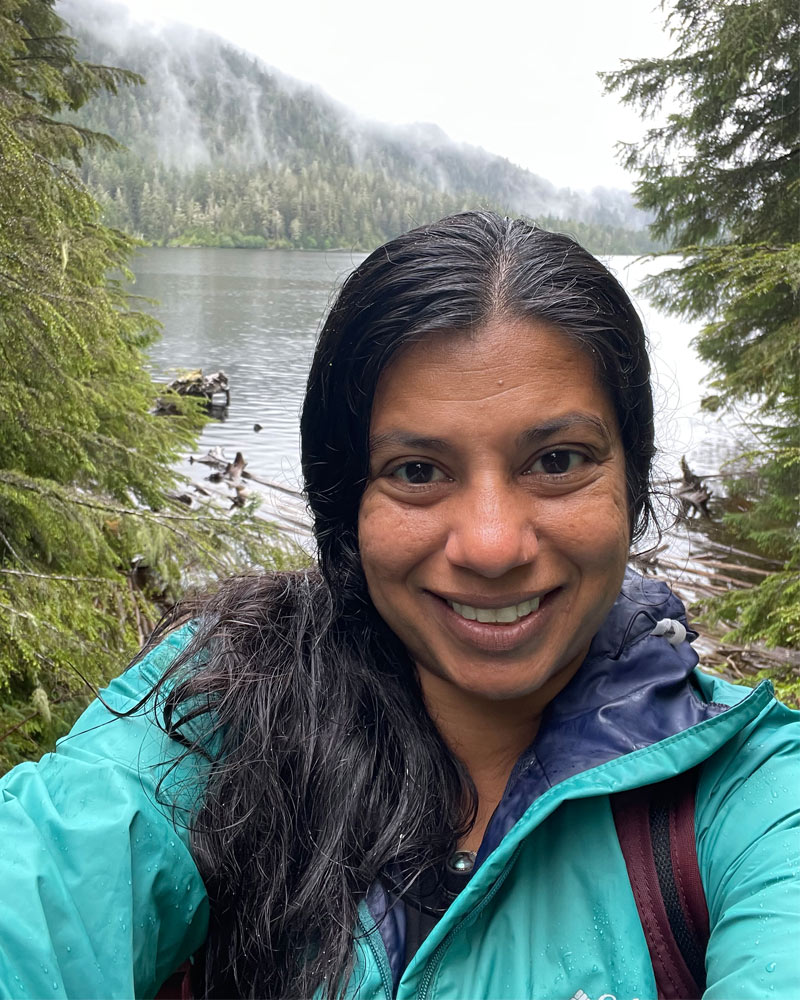 Nilam Vaughan, DO ’11, takes a selfie photo with a beautiful scenic background of Ketchikan, Alaska