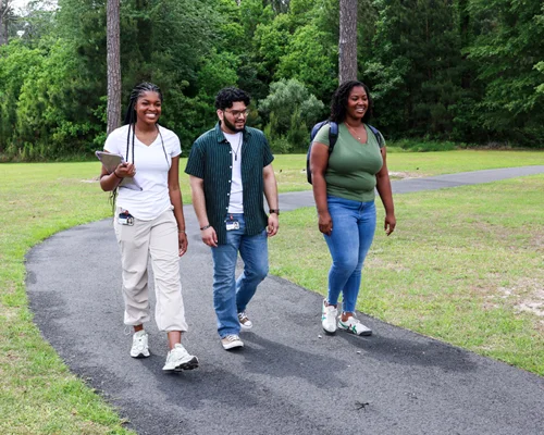 Students walk along a paved path in a wooded setting