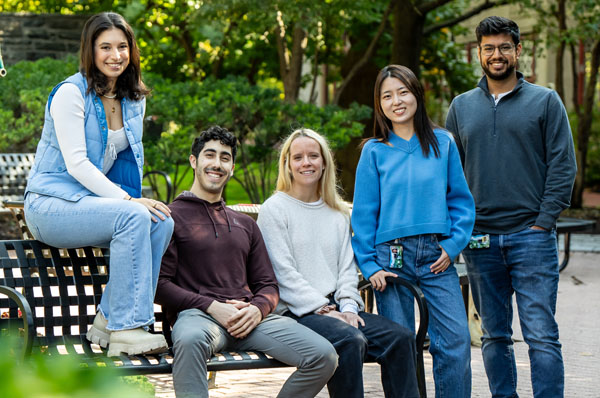 A group of diverse graduate students sitting on a bench smiling at PCOM's Philadelphia campus