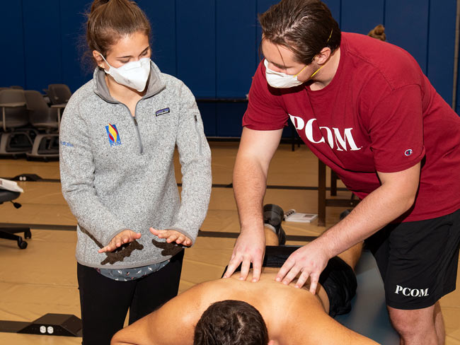 PCOM DO student receives OMT instruction from an OMM clinical scholar student.