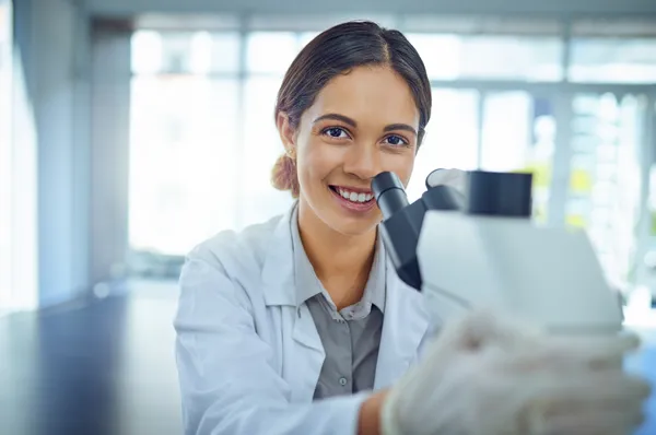 A biomed student smiles as they work with a microscope