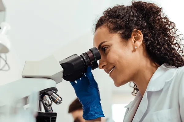 A biomed student smiles as they work with a microscope