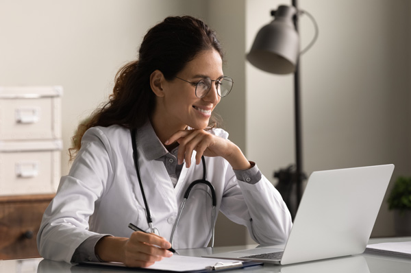 Physician smiling as she uses her latop to attend PCOM's geriatric medicine virtual CME course