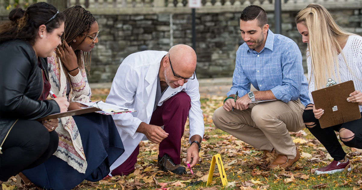 Forensic medicine students and faculty exploring a mock crime scene investigation site on the PCOM campus
