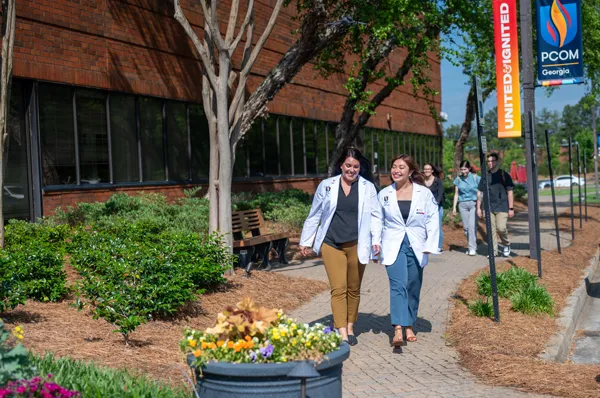 PCOM Georgia students in white lab coats walking along scenic walkway on campus grounds