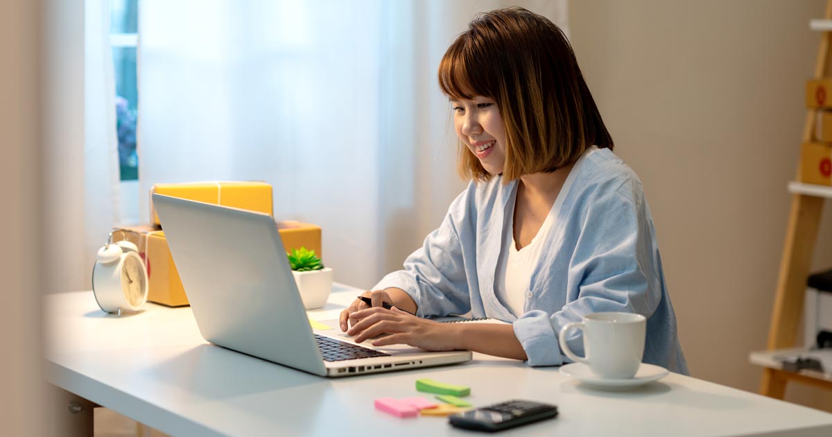A female student smiles as she works at a laptop computer while sitting at a desk.