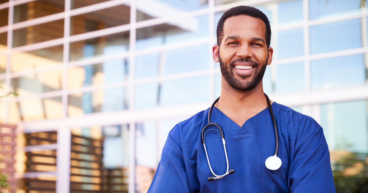 A PCOM physician assistant student smiles while standing in front of glass building