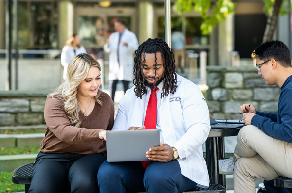 PCOM Doctor of Osteopathic Medicine students look at a laptop while sitting in the Philadelphia campus courtyard