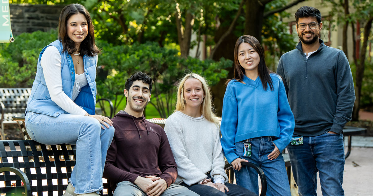 Five PCOM students sitting together on a bench