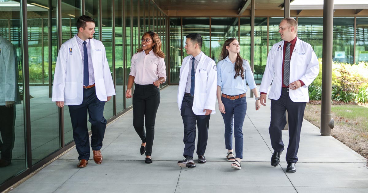 Five PCOM students in white coats walking together outside