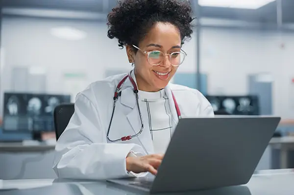 A PCOM Georgia pharmacy student smiles as she uses a laptop in a practice laboratory