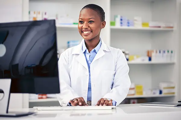 Young pharmacist stands at counter working on computer