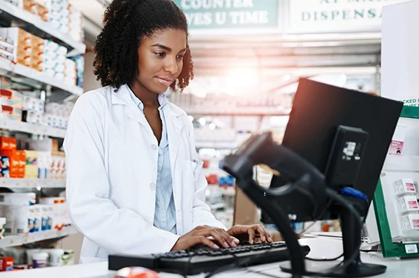 A PCOM Georgia pharmacy student smiles while using a computer in a dispensing lab