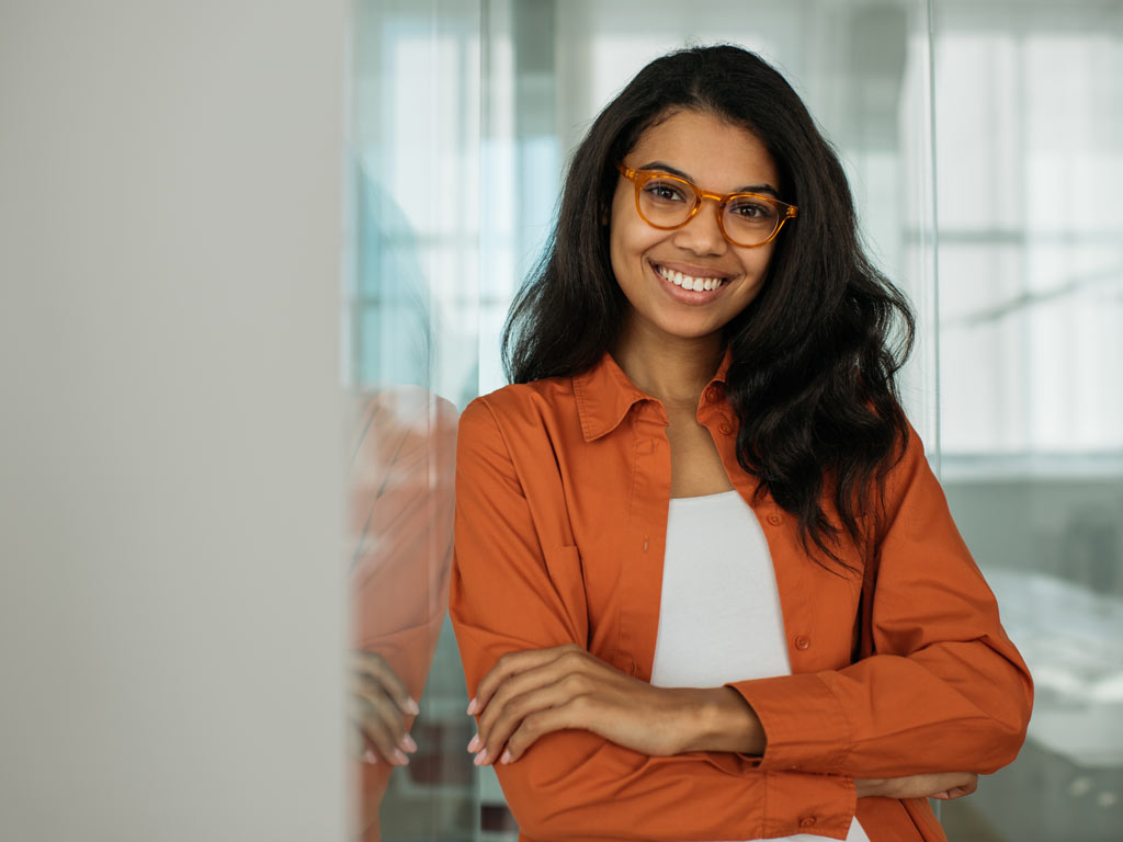 Female psychology student leaning against wall wearing glasses and an orange shirt