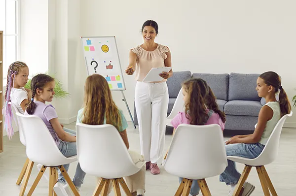 A counselor stands in front of five seated children