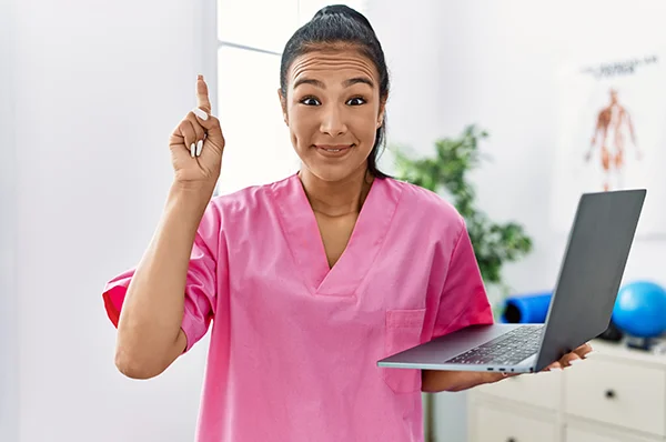 A physical therapy student smiles while holding a laptop