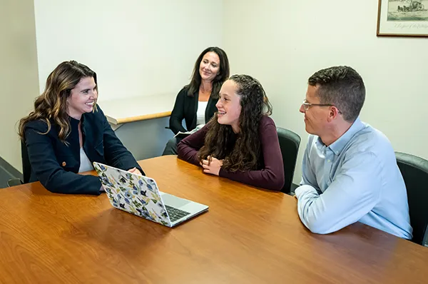 Three adults and a child sitting at a table looking at a laptop computer