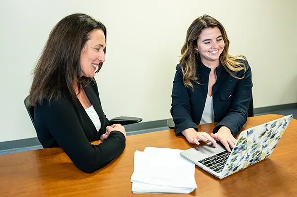 PCOM mental health counseling students smiling while working on a laptop in a study lounge