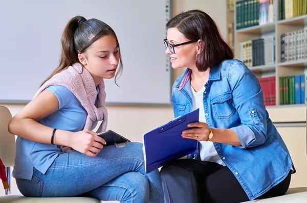 An adult and a child sitting in chairs reviewing notes on a clipboard
