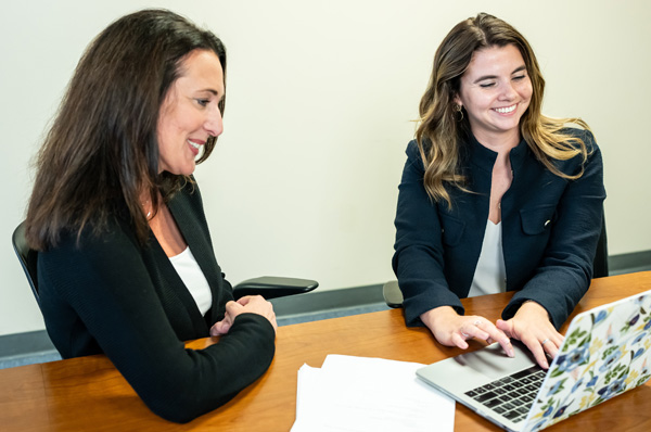 A PCOM school psychology student and facult member smile as they look at learning materials on a laptop computer