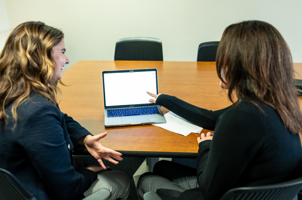 PCOM school psychology students and faculty smile as they sit at a table and use a laptop during a class