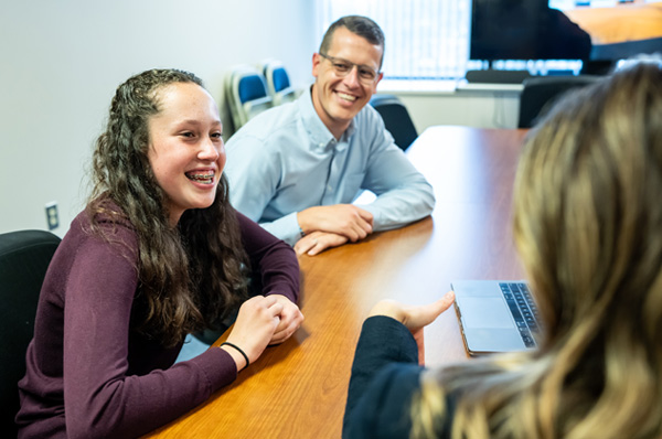 A high schooler and parent smile while working with a PCOM school psychology student