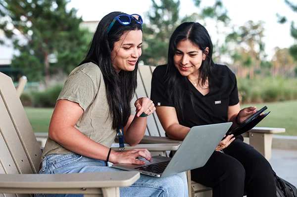 Students sit in patio chairs and look at their computers