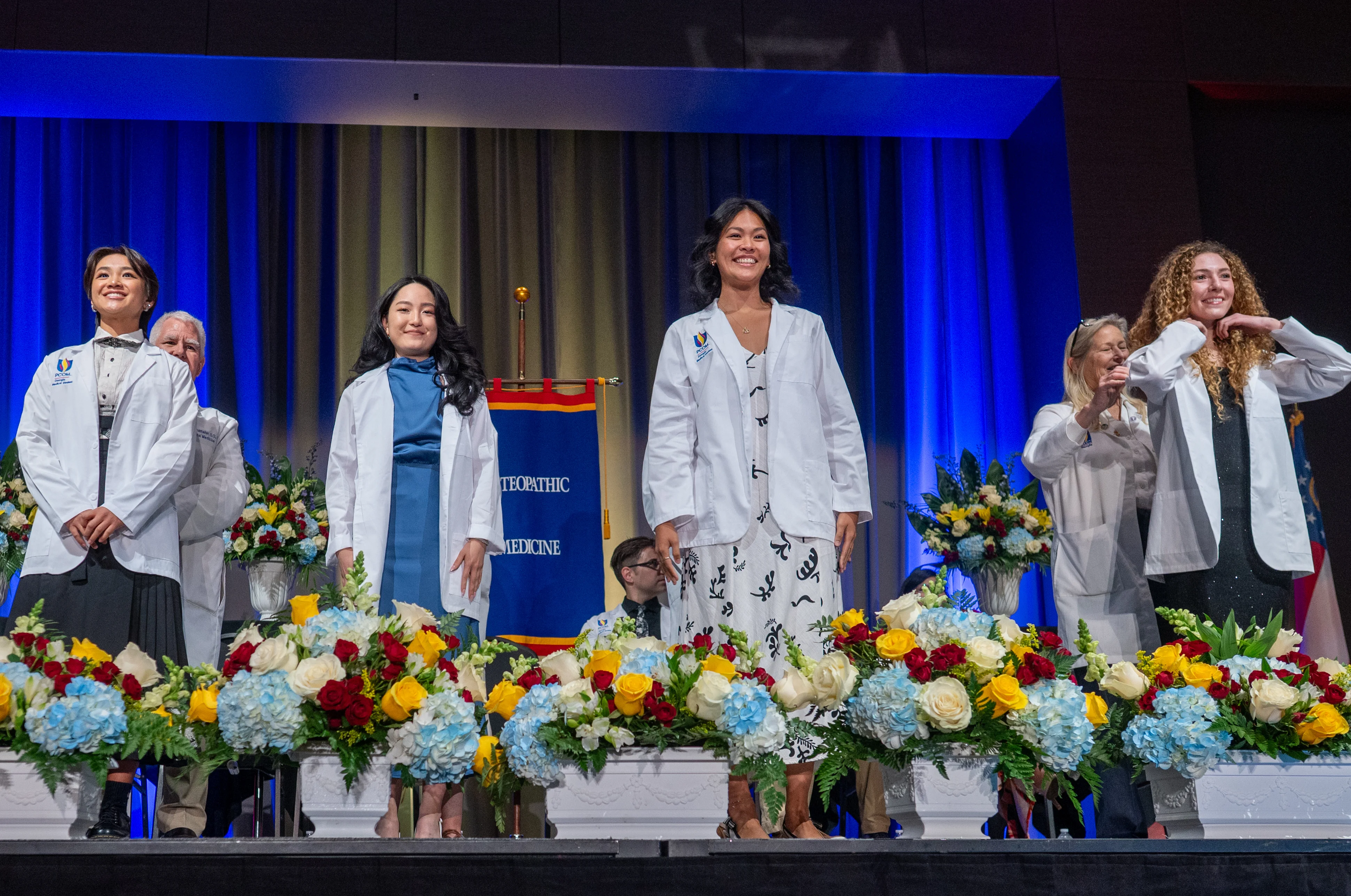 PCOM Georgia medical students smiling on stage while receiving their white coats from faculty